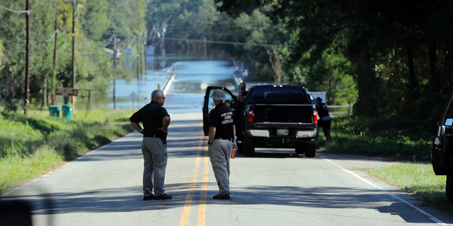 FILE - In this Wednesday, Sept. 19, 2018, file photo, responders congregate near where two people drowned the evening before when they were trapped in a Horry County Sheriff's transport van while crossing an overtopped bridge over the Little Pee Dee River on Highway 76, during rising floodwaters in the aftermath of Hurricane Florence in Marion County, S.C. Charges are expected to be filed Friday, Jan. 4, 2019, against two South Carolina law enforcement officers who were transporting two mental patients who drowned while locked in the back of a van during the hurricane. (AP Photo/Gerald Herbert, File)