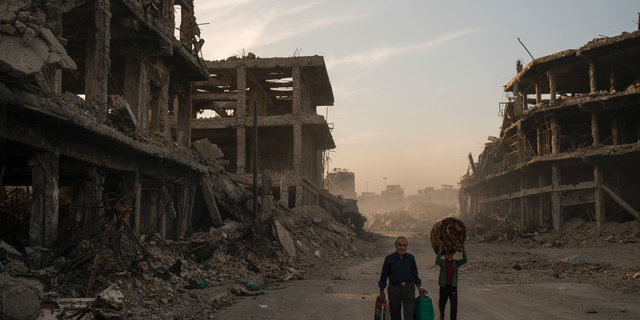 In this Nov. 15, 2017 file photo, Haider, left, and Abdullah carry belongings they collected from their damaged house to wash before returning to live in the Old City of Mosul, Iraq. (AP Photo/Felipe Dana)