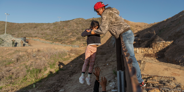 A migrant from Honduras pass a child to her father after he jumped the border fence to get into the U.S. side to San Diego, Calif., from Tijuana, Mexico, Thursday, Jan. 3, 2019. Discouraged by the long wait to apply for asylum through official ports of entry, many migrants from recent caravans are choosing to cross the U.S. border wall and hand themselves in to border patrol agents. (AP Photo/Daniel Ochoa de Olza)