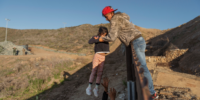 A migrant from Honduras pass a child to her father after he jumped the border fence to get into the U.S. side to San Diego, Calif., from Tijuana, Mexico, Thursday, Jan. 3, 2019. Discouraged by the long wait to apply for asylum through official ports of entry, many migrants from recent caravans are choosing to cross the U.S. border wall and hand themselves in to border patrol agents. (AP Photo/Daniel Ochoa de Olza)