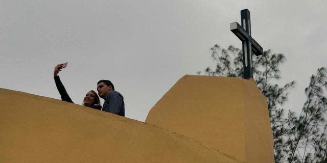 A couple pose for a photo backdropped by the cross crowning the newly consecrated Sagrado Corazon de Jesus Catholic church or Sacred Heart, in Sandino, Cuba, Saturday, Jan. 26, 2019. (AP Photo/Ramon Espinosa)