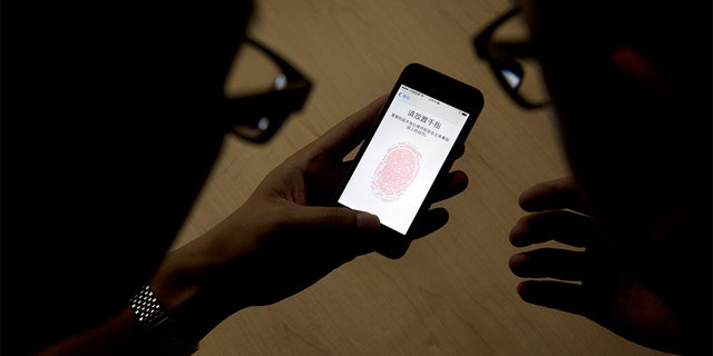 FILE - In this Sept. 11, 2013,  file photo, an Apple employee, right, instructs a journalist on the use of the fingerprint scanner technology built into the company's iPhone 5S during a media event in Beijing. The latest iPhones and Samsung Galaxy phones have fingerprint IDs that make it easier to unlock phones. Instead of typing in the four-digit passcode each time, you can tap your finger on the home button. (AP Photo/Ng Han Guan, File)