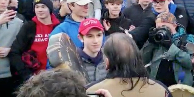 This Friday, Jan. 18, 2019 image shows Nicholas Sandmann staring at Nathan Phillipps, the Native American man who approached him banging a drum. (Survival Media Agency via AP)