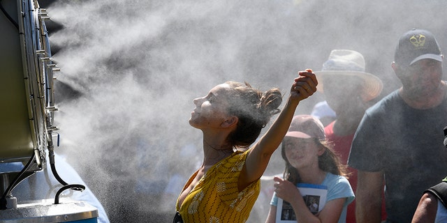 Spectators cool themselves down with a water mist fan during play on day one at the Australian Open tennis championships in Melbourne, Australia, Monday, Jan. 14, 2019.
