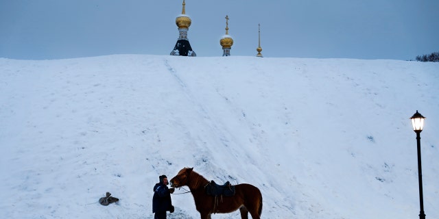 A man prepares a horse to ride tourists during a cold winter day at a hill, near the Assumption Cathedral in the small Russian town of Dmitrov.