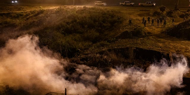 Migrants run as tear gas is thrown by U.S. Border Protection officers to the Mexican side of the border fence after they climbed the fence to get to San Diego on Tuesday. (Associated Press)