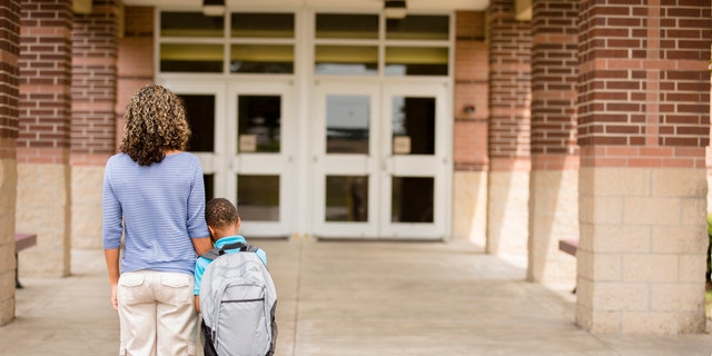 A little boy clings to his mom for reassurance on the first day of school.