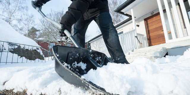 Man removing snow with a snow shovel in front of his house.