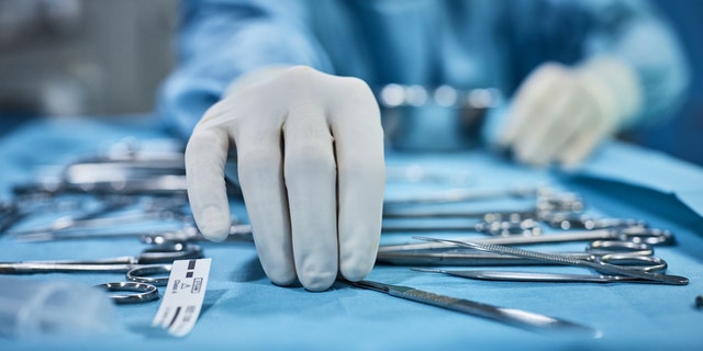 A surgeon picks up surgical tools from tray before a surgery in a hospital operating room. 