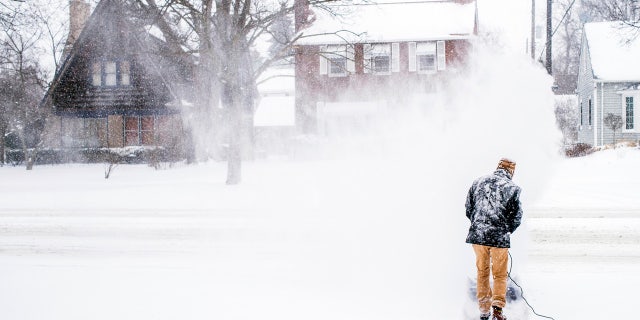 Stephen Johnson clears snow off his neighbor's driveway into Court Street during a winter snowstorm on Monday, Jan. 28, 2019, in Flint, Mich.