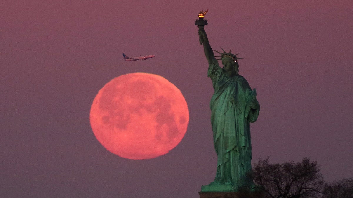 The Super Snow Moon sets behind the Statue of Liberty as the sun rises on February 19, 2019, in New York City.