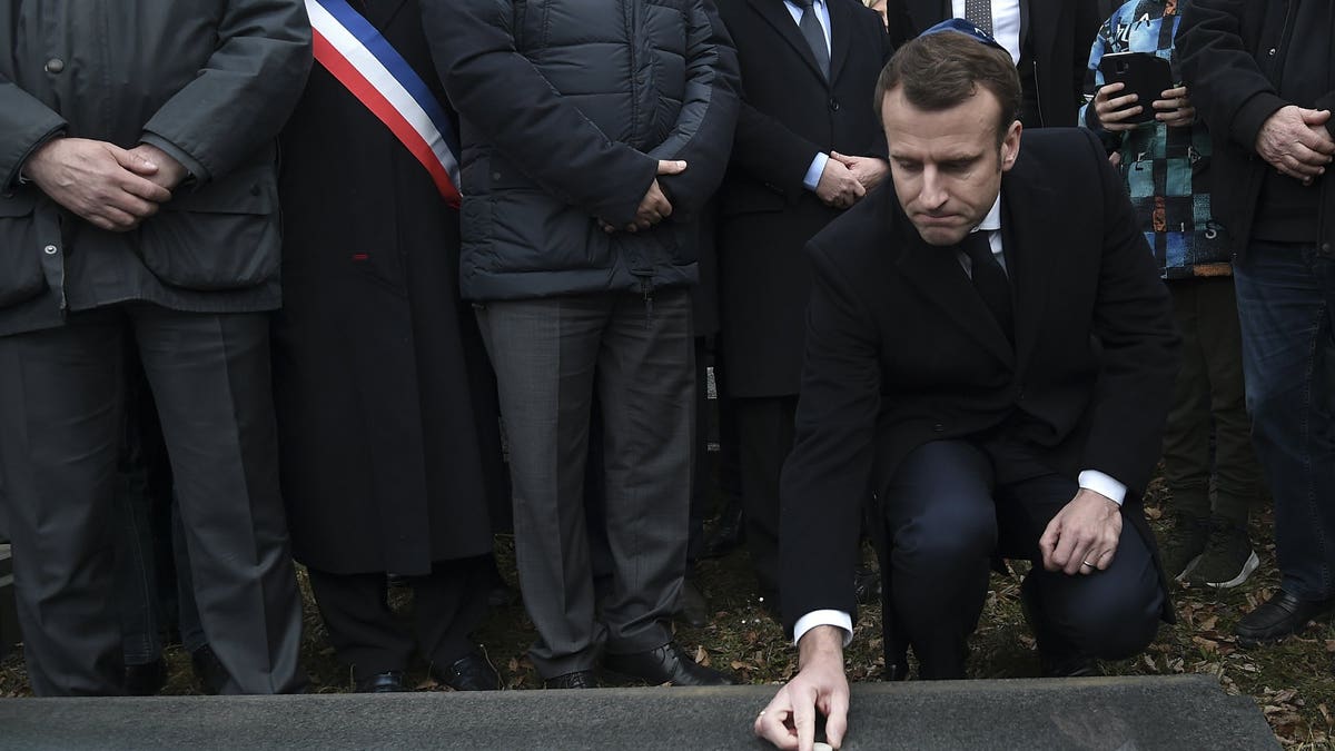French President Emmanuel Macron puts a stone on a vandalized grave in a show of respect during a visit at the Jewish cemetery in Quatzenheim, eastern France, Tuesday Feb. 19, 2019. French residents and public officials from across the political spectrum geared up Tuesday for nationwide rallies against anti-Semitism following a series of anti-Semitic acts, including the swastikas painted on about 80 gravestones at the Jewish cemetery overnight.
