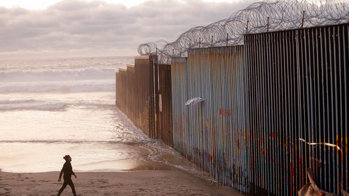 FILE - In this Jan. 9, 2019 file photo, a woman walks on the beach next to the border wall topped with razor wire in Tijuana, Mexico. (AP Photo/Gregory Bull, File)