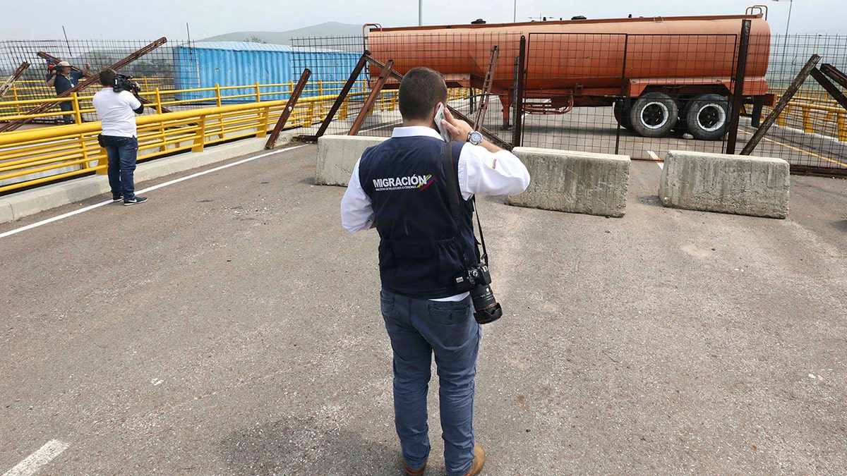 An immigration official observes a fuel tanker, cargo trailers and makeshift fencing, used as barricades by Venezuelan authorities attempting to block humanitarian aid entering from Colombia on the Tienditas International Bridge.