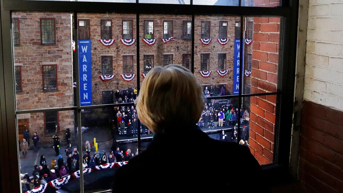 Sen. Elizabeth Warren, D-Mass., looks out a window at Everett Mills as a crowd gathers for an event where she formally launched her presidential campaign, Saturday, Feb. 9, 2019, in Lawrence, Mass. (AP Photo/Elise Amendola)