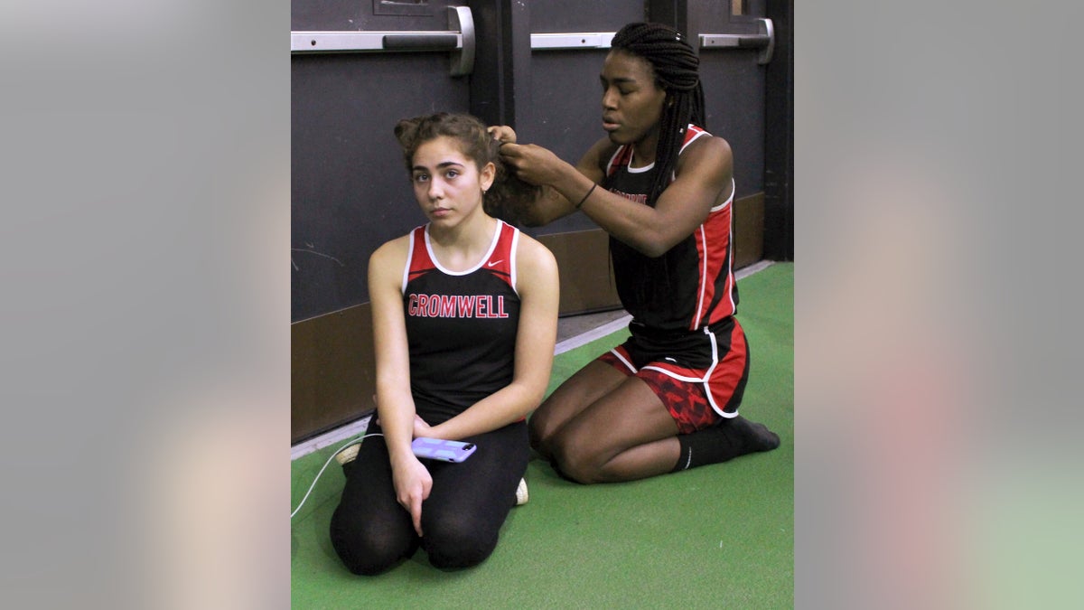 In this Thursday, Feb. 7, 2019 photo, Cromwell High School transgender athlete Andraya Yearwood , right, braids the hair of teammate Taylor Santos, left, during a break at a track meet at Hillhouse High School in New Haven, Conn. Yearwood, a 17-year-old junior at Cromwell High School, is one of two transgender high school sprinters in Connecticut, transitioning to female. (AP Photo/Pat Eaton-Robb)