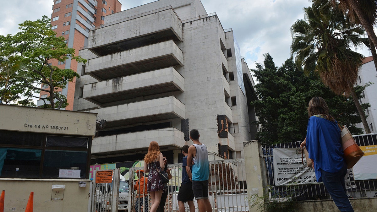 People look at the six-floor apartment building that former cartel boss Pablo Escobar once called home, in Medellin, Colombia, Friday, Feb. 22, 2019. The white concrete building in Medellin's leafy Poblado neighborhood was gutted by a car bomb in 1988 and has remained an unoccupied eyesore ever since, drawing mostly foreign tourists who sign up every day for tours of Escobar's former hometown haunts. The Netflix "Narcos" series has also popularized such attractions. It was demolished on Friday. (AP Photo/Luis Benavidez)