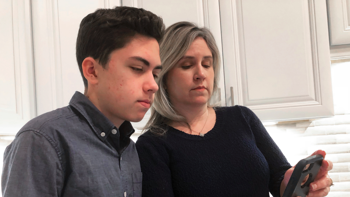 Grant Thompson and his mother, Michele, look at an iPhone in the family's kitchen in Tucson, Ariz., on Thursday, Jan. 31, 2019.  (AP Photo/Brian Skoloff)