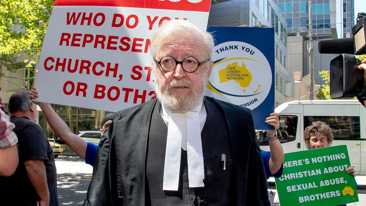 Cardinal George Pell's lawyer Robert Richter leaves the County Court as protesters hold placards in Melbourne, Australia, Wednesday, Feb. 27, 2019. The most senior Catholic cleric ever convicted of child sex abuse could face his first night in custody after a sentencing hearing Wednesday that will decide his punishment for molesting two choirboys in a Melbourne cathedral two decades ago. (AP Photo/Andy Brownbill)