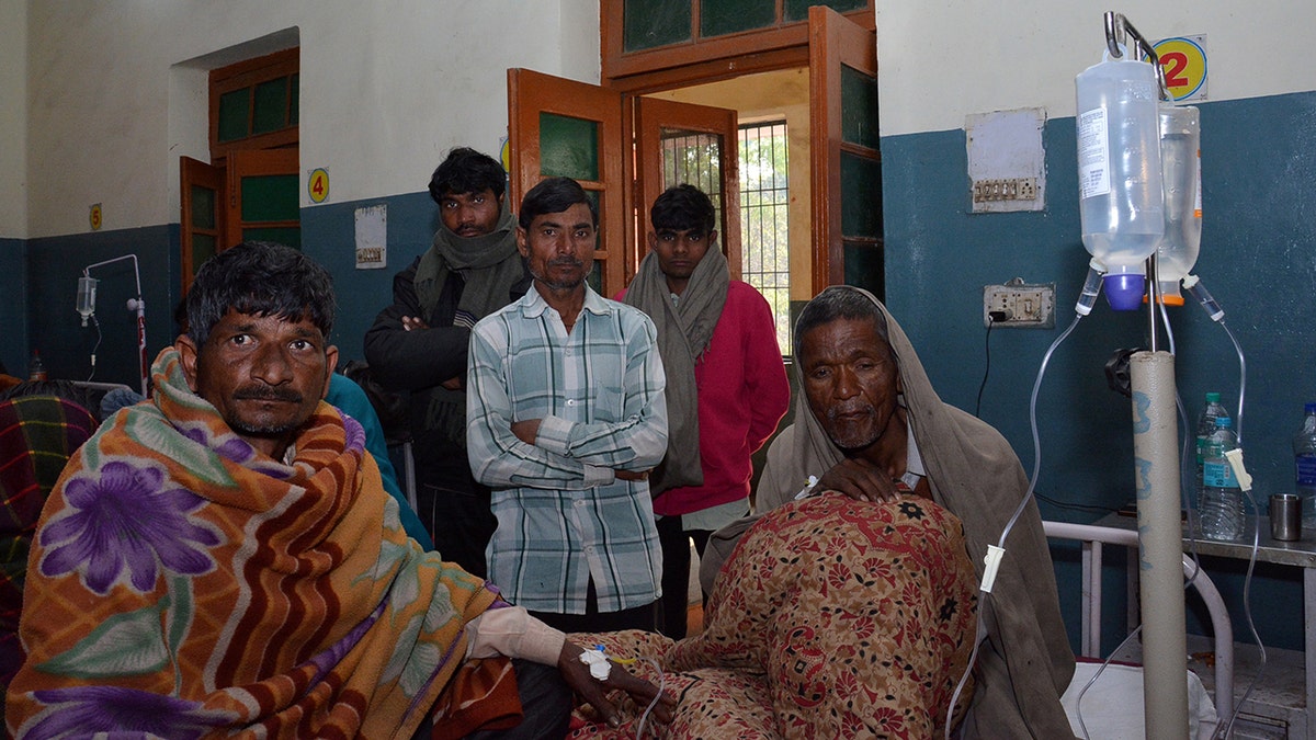 Two men who consumed bootleg alcohol, sit on a hospital bed as relatives look on, in Saharanpur, northern state of Uttar Pradesh, India February 11, 2019. REUTERS/Stringer - RC1A90540A20