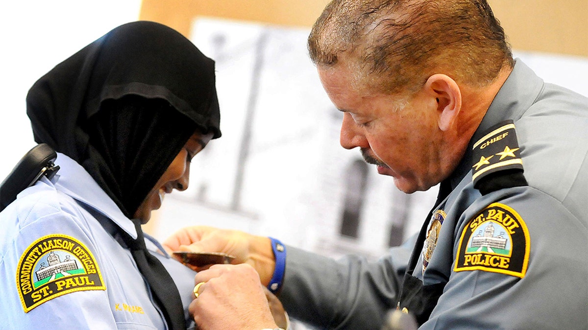 In this March 1, 2014 file photo, St. Paul, Minn. Community Officer Kadra Mohamed, left, smiles as she receives her badge from St. Paul, Minn. Police Chief Thomas Smith, during a ceremony for her and the East African Junior Police Academy at the Western District Police Station in St. Paul, Minn. (Sherri LaRose-Chiglo/Pioneer Press via AP)