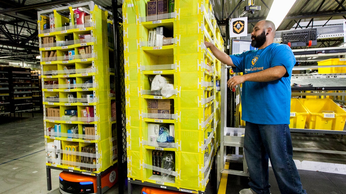 An Amazon fulfillment center employee is seen above, working with a robot.