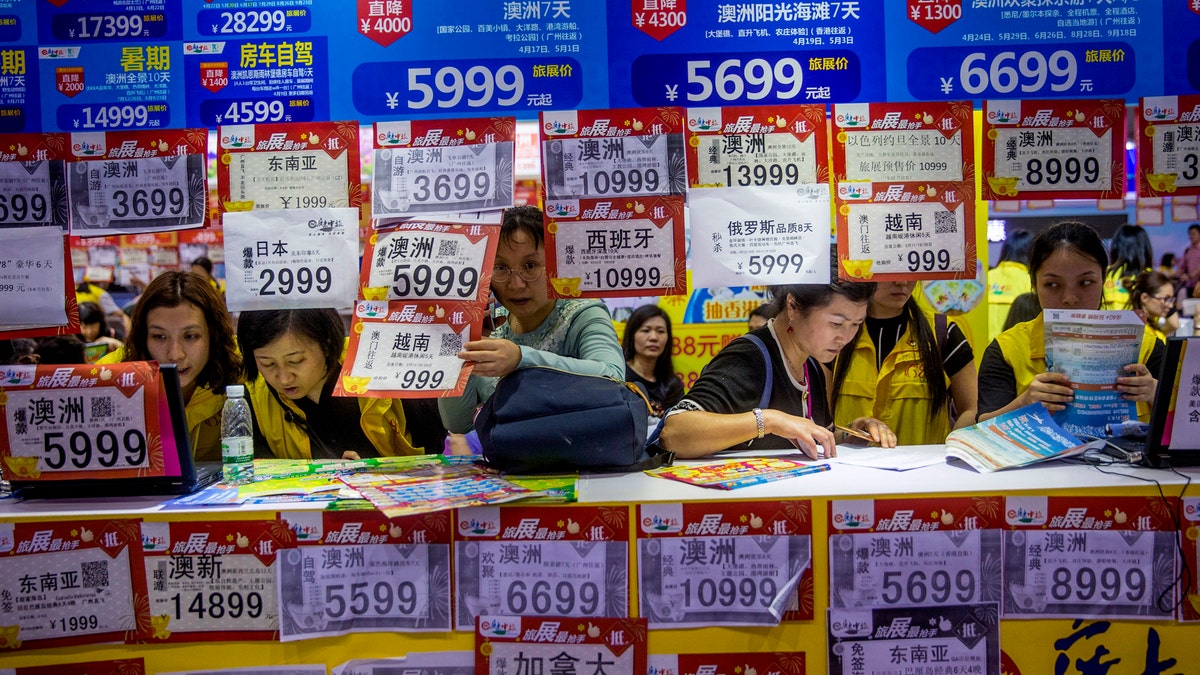 In this March 3, 2018, photo, people check on travel packages offered by travel agencies during the Guangzhou International Travel Fair in Guangzhou in south China's Guangdong province. Travelers in China were blocked from buying plane tickets 17.5 million times last year as a penalty for failing to pay fines or other offenses. The Chinese government reported this week on penalties imposed under a controversial "social credit" system the ruling Communist Party says will improve public behavior. (Chinatopix via AP)