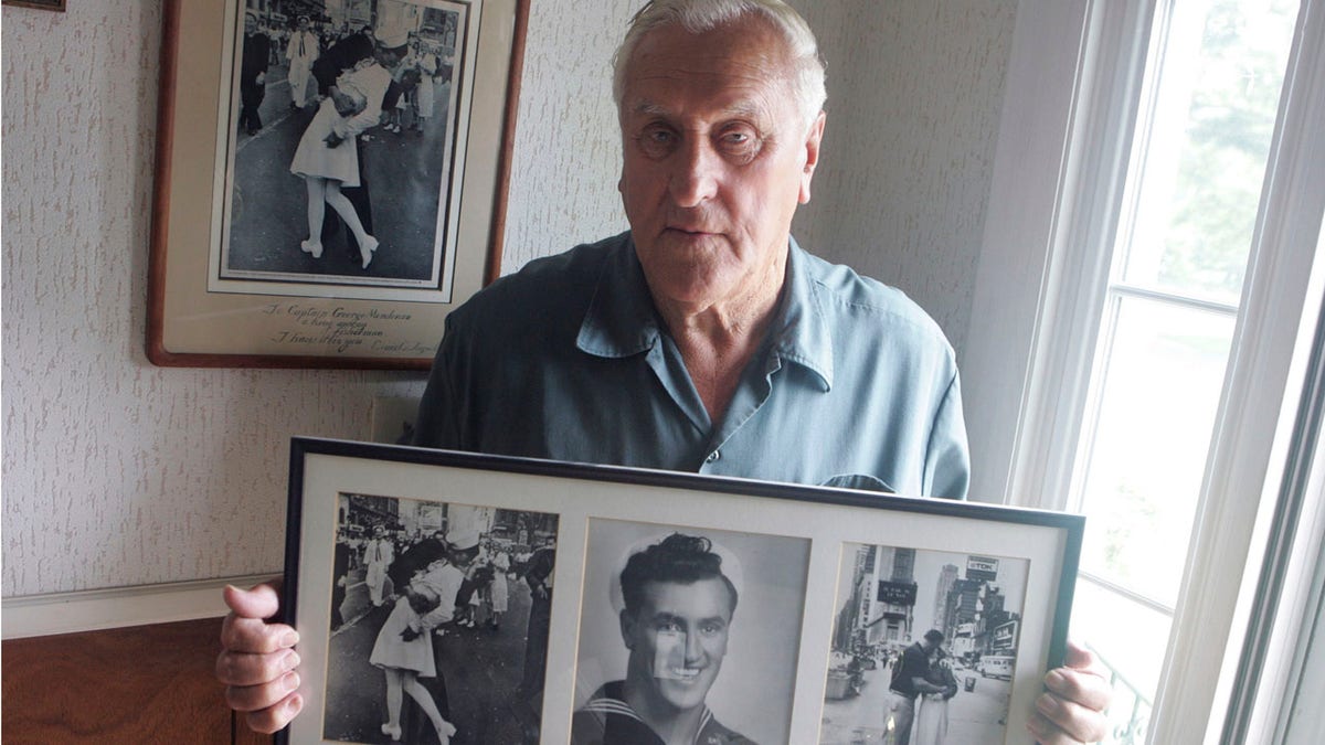 In this July 2, 2009, photo George Mendonsa poses for a photo in Middletown, R.I., holding a copy of the famous Alfred Eisenstadt photo of Mendonsa kissing a woman in a nurse's uniform in Times Square on Aug. 14, 1945, while celebrating the end of World War II, left. Mendonsa died Sunday, Feb. 17, 2019, he was 95.