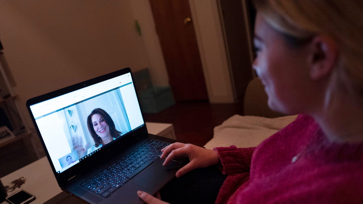 In this Jan. 14, 2019 photo, Caitlin Powers sits in the living room of her Brooklyn apartment in New York, and has a telemedicine video conference with physician, Dr. Deborah Mulligan. Widespread smartphone use, looser regulations and employer enthusiasm are helping to expand access to telemedicine, where patients interact with doctors and nurses from afar, often through a secure video connection. (AP Photo/Mark Lennihan)