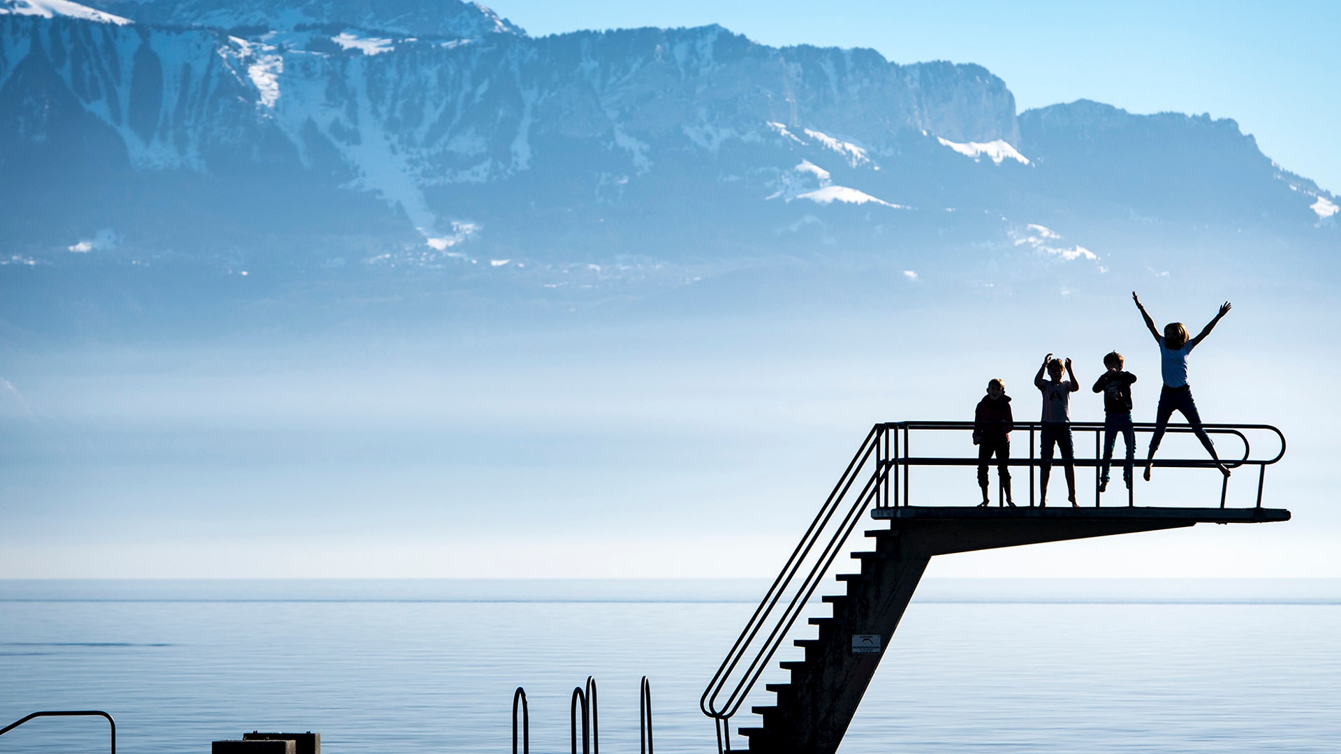 Kids enjoy the sunny warm weather on a diving platform on the shore of the Lake Geneva in front of the Swiss and French Alps in Lutry, Switzerland, Feb. 16, 2019. 
