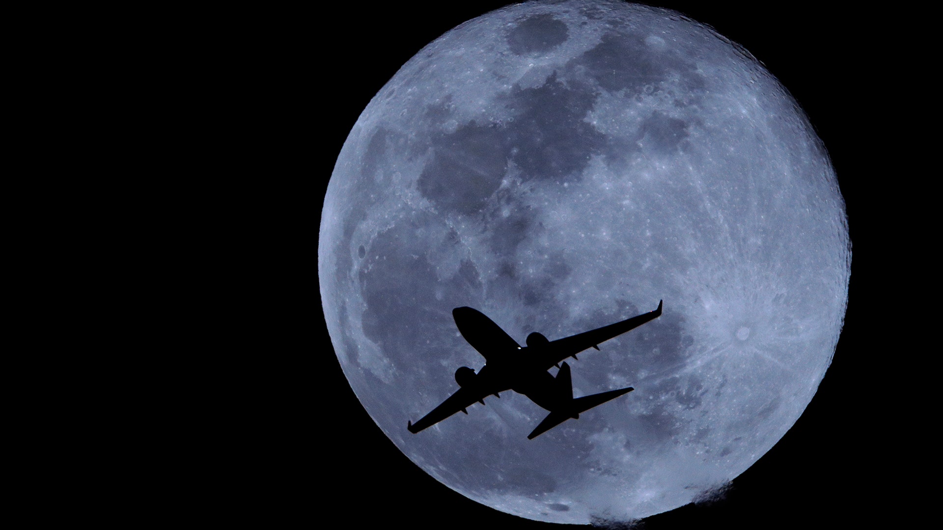 A passenger jet is silhouetted against the rising full moon as it takes off from Sky Harbor airport in Phoenix, Ariz., Feb. 19, 2019. 
