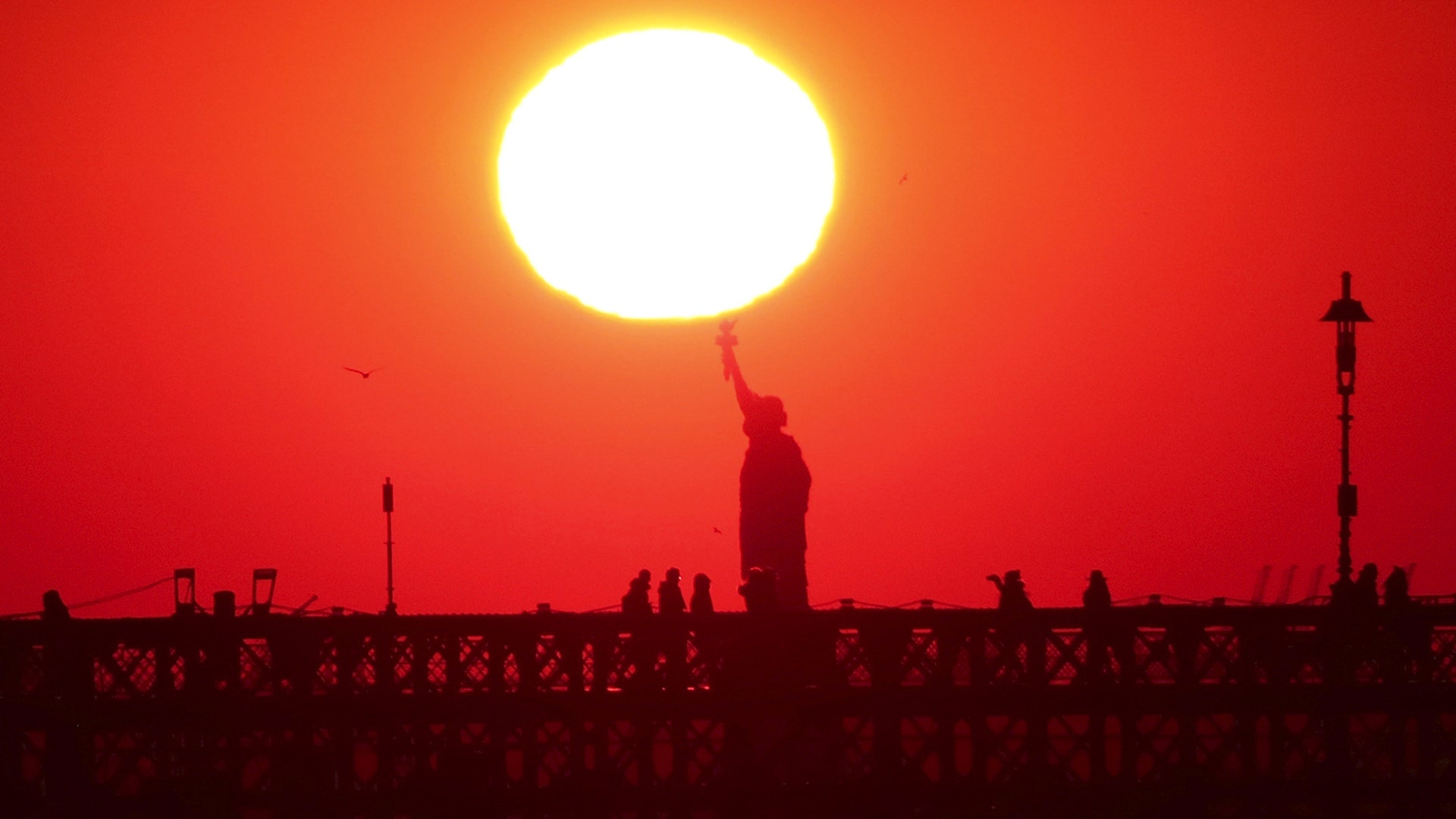The sun sets behind the Statue of Liberty and the Brooklyn Bridge in New York City, January 28, 2019.