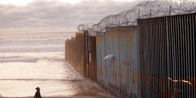   FILE - In this photo In the archives of January 9, 2019, a woman walks on the beach next to the border wall topped with razor wire in Tijuana, Mexico. (Photo AP / Gregory Bull, File) 