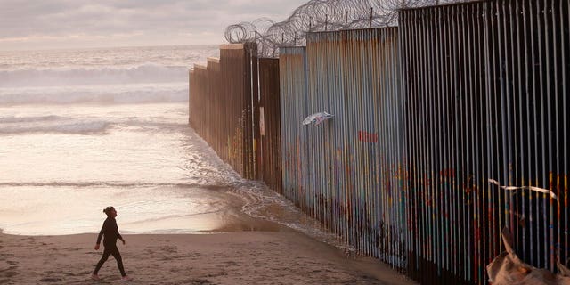 FILE - In this Jan. 9, 2019 file photo, a woman walks on the beach next to the border wall topped with razor wire in Tijuana, Mexico. (AP Photo/Gregory Bull, File)