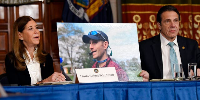 FILE - In this Tuesday, Jan. 29, 2019, file photo, Linda Beigel Schulman, left, holds a photograph of her son Scott Beigel, who was killed during the Valentine’s Day massacre at Marjory Stoneman Douglas High School, while speaking with New York Gov. Andrew Cuomo and gun safety advocates during a news conference at the state Capitol in Albany, N.Y. Since the shooting, states have seen a surge of interest in laws intended to make it easier to disarm people who show signs of being violent or suicidal. (AP Photo/Hans Pennink, File)