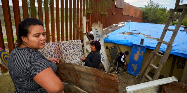 FILE - In this Jan. 16, 2019, file photo, Yuli Arias, left, stands near a newly-replaced section of the border wall as her mother, Esther Arias, center, stands in the family's house that was once threatened by construction along the border in Tijuana, Mexico. The Trump administration said Thursday, Feb. 7, 2019, it would waive environmental reviews to replace up to 14 miles (22.5 kilometers) of border barrier in San Diego, shielding itself from potentially crippling delays. (AP Photo/Gregory Bull, File)