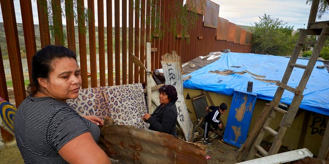 FILE - In this Jan. 16, 2019, file photo, Yuli Arias, left, stands near a newly-replaced section of the border wall as her mother, Esther Arias, center, stands in the family's house that was once threatened by construction along the border in Tijuana, Mexico. The Trump administration said Thursday, Feb. 7, 2019, it would waive environmental reviews to replace up to 14 miles (22.5 kilometers) of border barrier in San Diego, shielding itself from potentially crippling delays. (AP Photo/Gregory Bull, File)
