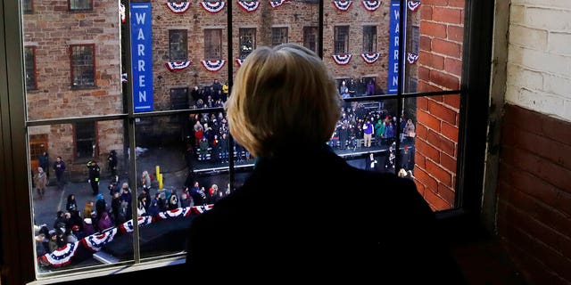 Sen. Elizabeth Warren, D-Mass., looks out a window at Everett Mills as a crowd gathers for an event where she formally launched her presidential campaign, Saturday, Feb. 9, 2019, in Lawrence, Mass. (AP Photo/Elise Amendola)
