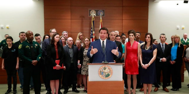 Joined by officials and family members of victims of the Parkland, Fla., school shooting, Gov. Ron DeSantis speaks during a news conference on Wednesday in Fort Lauderdale. DeSantis is calling for a statewide grand jury to look at whether the state's 67 school districts are following school safety laws enacted in the wake of a high school massacre.