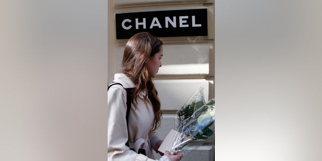 A well-wisher arrives with a bunch of flowers at Chanel's headquarters in Paris, to pay tribute to fashion designer Karl Lagerfeld, France, Tuesday, Feb. 19, 2019. Chanel's iconic couturier, Karl Lagerfeld, whose accomplished designs as well as trademark white ponytail, high starched collars and dark enigmatic glasses dominated high fashion for the past 50 years, has died. He was around 85 years old. (AP Photo/Michel Euler)