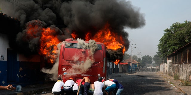 Demonstrators push a bus that was torched during clashes with the Bolivarian National Guard in Urena, Venezuela