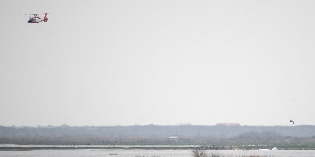 A helicopter flies overhead as emergency personnel work the scene of a plane crash site in Trinity Bay in Anahuac, Texas on Saturday, Feb. 23, 2019. (Brett Coomer/Houston Chronicle via AP)