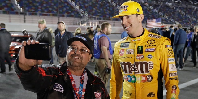 Kyle Busch, right, poses for a selfie photo with a race fan before the first of two qualifying auto races for the NASCAR Daytona 500 at Daytona International Speedway, Thursday, in Daytona Beach, Fla. (AP Photo/John Raoux)