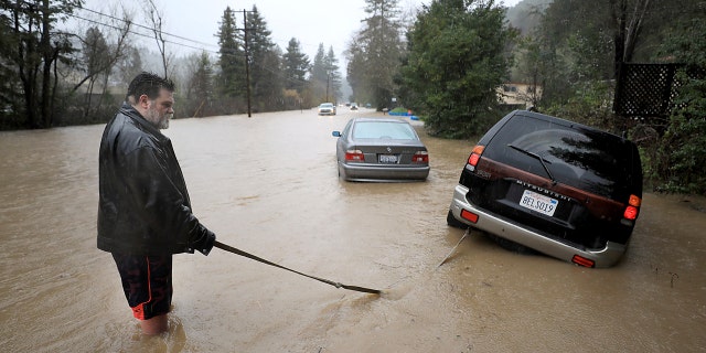 Tim Russell of Guerneville is trying to pull a motorist from Armstrong Woods Road after his flood in Guerneville, California on Tuesday, February 26, 2019.