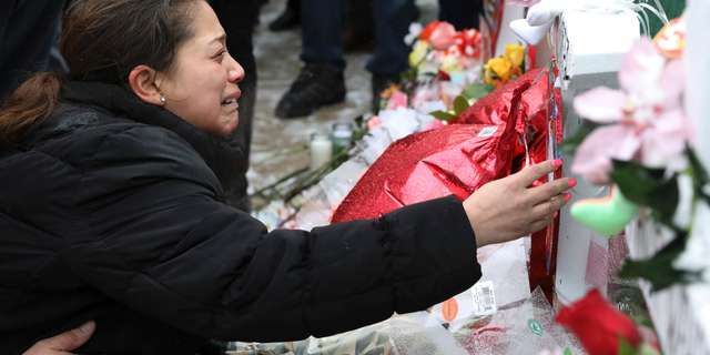 One of victim Vicente Juarez's daughter Diana Juarez cries as she touch a cross at a makeshift memorial Sunday, Feb. 17, 2019, in Aurora, Ill., near Henry Pratt Co. manufacturing company where several were killed on Friday. Authorities say an initial background check five years ago failed to flag an out-of-state felony conviction that would have prevented a man from buying the gun he used in the mass shooting in Aurora. (AP Photo/Nam Y. Huh)
