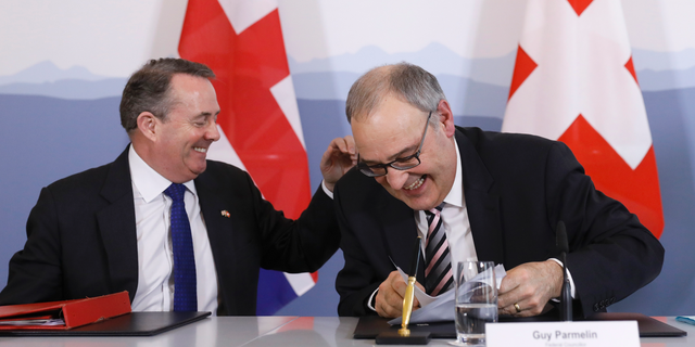 Swiss Federal Councillor Guy Parmelin, right, and British Secretary of State for International Trade Liam Fox, left, react after signing a trade agreement in Bern, Switzerland, Monday, Feb. 11, 2019. Parmelin and Fox signed a bilateral trade agreement regulating relations between the two countries after the Brexit. Because of the customs treaty with Switzerland, the agreement also applies to Liechtenstein. (Peter Klaunzer/Keystone via AP)