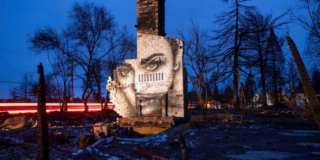 In this Feb. 8, 2019, photo, a mural by artist Shane Grammer adorns the chimney of a residence leveled by the Camp Fire in Paradise, Calif. Grammer says he painted murals throughout the fire-ravaged town to convey hope in the midst of destruction. In the 100 days since a wildfire nearly burned the town of Paradise off the map, the long recovery is just starting. Work crews have been cutting down trees and clearing burned-out lots, but Paradise is mostly a ghost town where survivors still dig for keepsakes in the foundations of their homes. (AP Photo/Noah Berger)