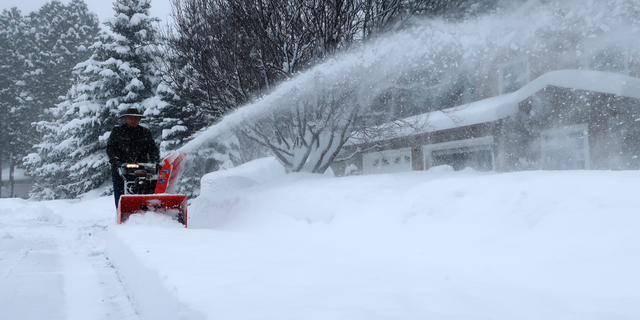 Richard Henn runs a snow blower down the sidewalk outside his home in Flagstaff, Arizona, on Thursday, Feb. 21, 2019. Schools across northern Arizona canceled classes and some government offices decided to close amid a winter storm that's expected to dump heavy snow in the region. (AP Photo/Felicia Fonseca)