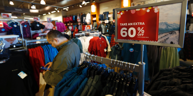 FILE- In this Dec. 24, 2018, photo a last-minute shopper scans his mobile device next to a sign marking discounts on coats at Columbia store as shoppers finish up their Christmas gift lists at the Outlet Malls in Castle Rock in Castle Rock, Colo. The On Thursday, Feb. 14, 2019, the Commerce Department releases U.S. retail sales data for December. (AP Photo/David Zalubowski, File)