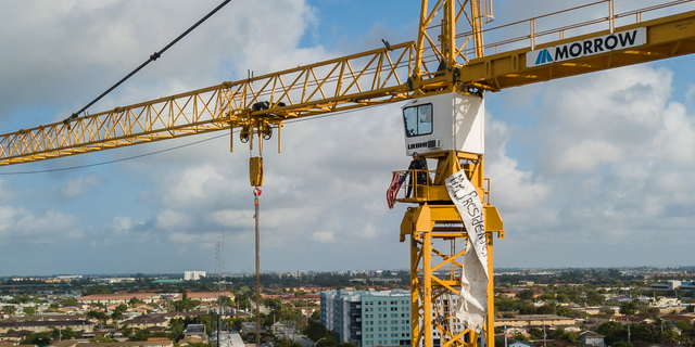A man stands inside a construction crane where he attached an American flag and a banner near Florida International University in Sweetwater, Fla., Monday, Feb. 18, 2019. President Donald Trump is scheduled to host a rally at the school in the afternoon. (Matias J. Ocner/Miami Herald via AP)